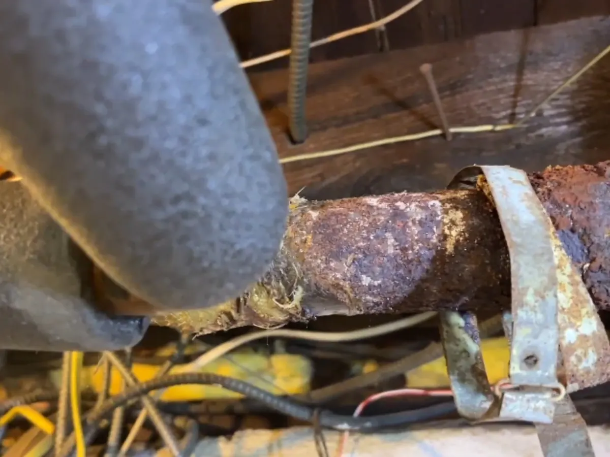 Heavily rusted galvanized supply pipe hanging from a metal strap